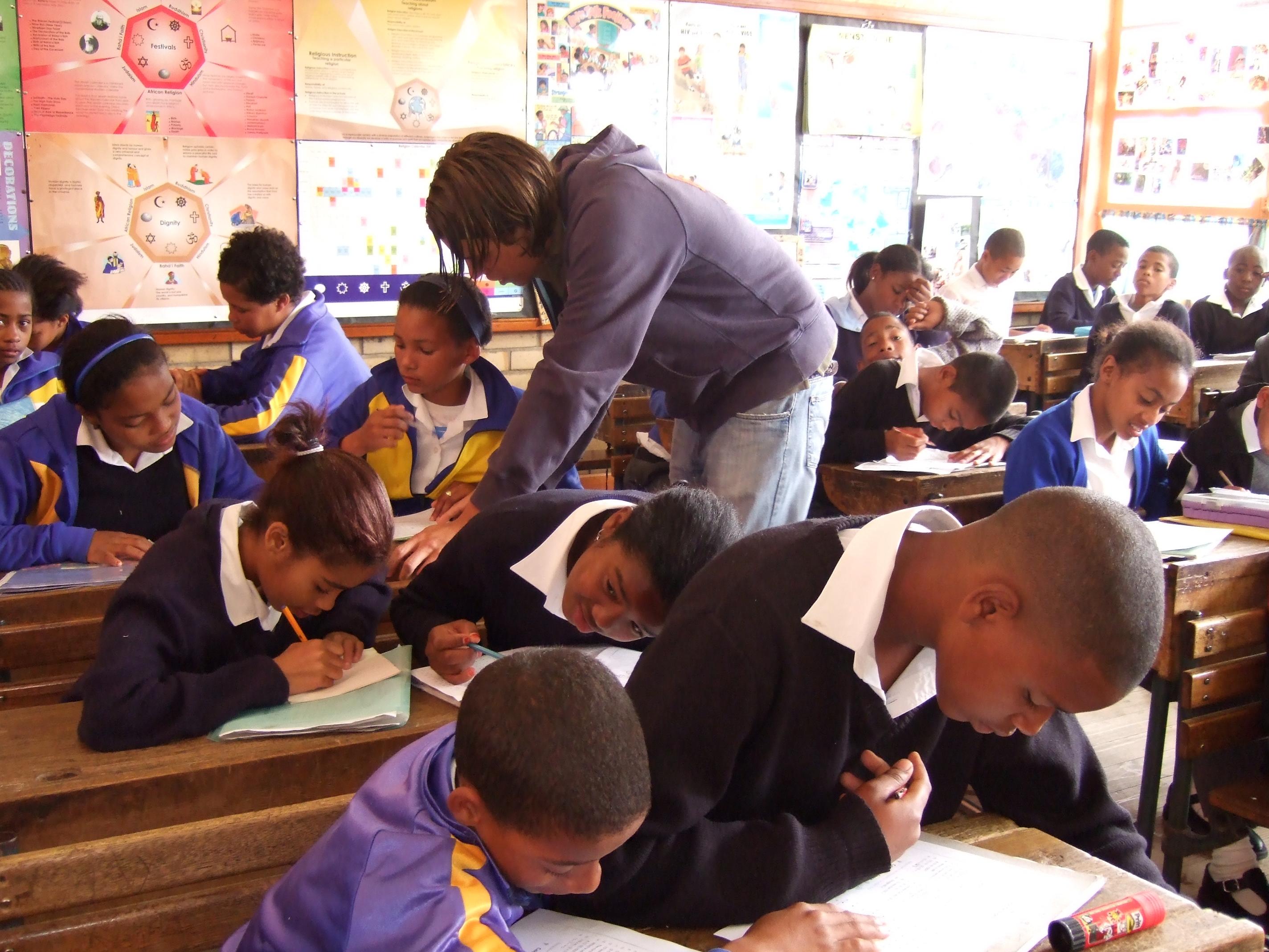 Projects Abroad volunteer working as a teacher in South Africa goes around the classroom to help her students with their classwork Students complete their classroom exercise while a volunteer assists during her teaching work experience in South Africa